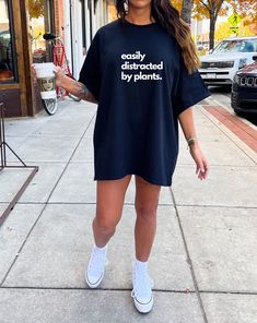 a woman standing on the sidewalk wearing a t - shirt that says stay busy, distracted by plants