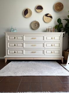 a white dresser with baskets on the wall above it and a rug in front of it