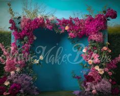 a blue backdrop with pink and white flowers on the side, surrounded by greenery