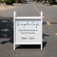 a white sign sitting on the side of a road next to a street with trees