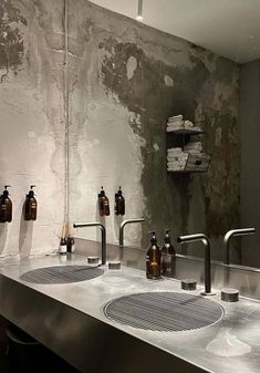 two sinks with soap dispensers in front of a wall covered in cement