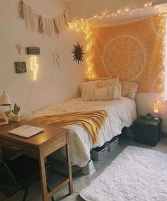 a room with a bed, desk and lights on the wall above it in front of a window