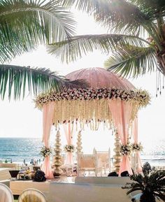 an outdoor wedding setup with pink draping and white flowers on the canopy, surrounded by palm trees