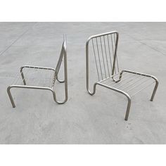 two metal chairs sitting next to each other on top of a cement ground with no one in it