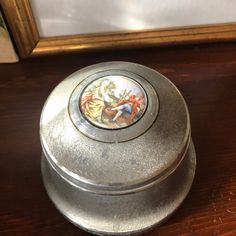 an old metal container with a painting on the lid sitting on a wooden table next to a mirror