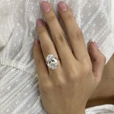 a woman's hand with a diamond ring on her left hand, wearing a white dress