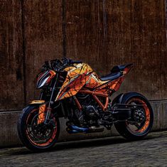 an orange and black motorcycle parked in front of a wooden wall with graffiti on it