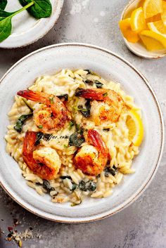 pasta with shrimp and spinach in a white bowl next to lemon wedges on the side