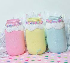 three pastel jars with sprinkles on them are sitting on a table