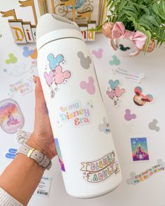 a person holding onto a white water bottle with mickey and minnie mouse stickers on it