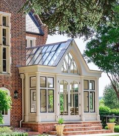 an orangery in front of a brick building with white trim and windows on the roof