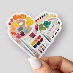 a hand holding up a heart shaped sticker with lots of different colors on it