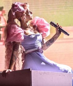 two women dressed in pink and blue are on stage with one holding a microphone to her ear