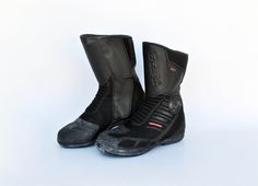 a pair of black motorbike boots sitting on top of a white floor next to each other