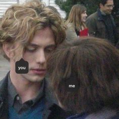 a young man with curly hair is talking to someone on his cell phone while standing in front of other people