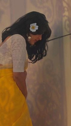 a woman in a yellow skirt and white top with a flower in her hair standing next to a wall