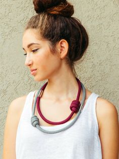 a woman wearing a white shirt and a red rope necklace with grey beads on her neck