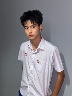 a young man standing in front of a wall wearing a white shirt and blue shorts