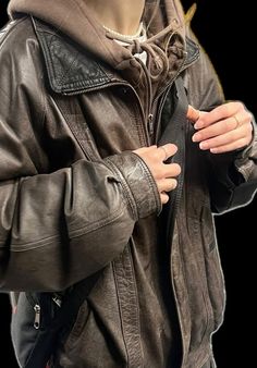 a man in a leather jacket is holding his hand on his pocket and looking at the camera