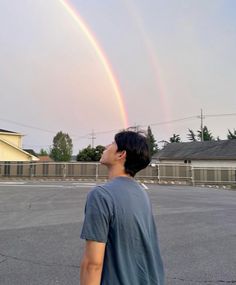 a man standing in an empty parking lot with a rainbow in the sky behind him