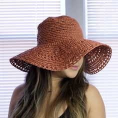 a woman wearing a brown crochet hat with long hair in front of a window