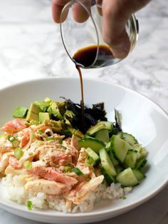 someone is pouring sauce over rice with cucumbers and other vegetables on the plate