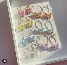 several pairs of earrings with bows on them are displayed in a white box next to a pink wall