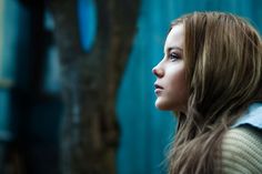 a woman with long hair standing in front of a tree looking off into the distance