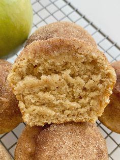 a close up of some doughnuts on a cooling rack with an apple in the background