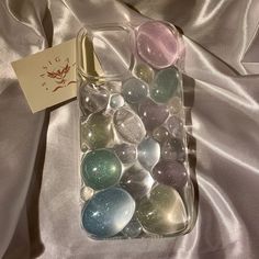 a glass container filled with lots of different colored marbles next to a tag on a silver satin surface