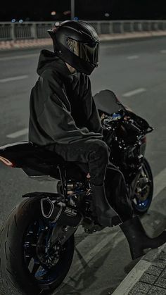 a man riding on the back of a black motorcycle down a street at night time