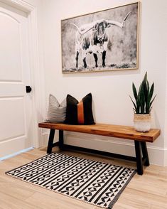 a wooden bench sitting in front of a painting on the wall next to a potted plant