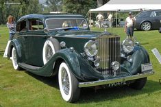 an antique car is parked on the grass at a car show with people standing around