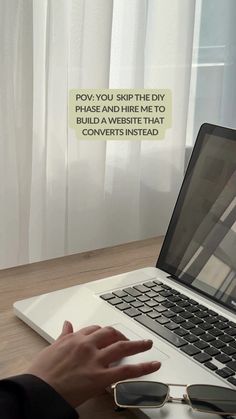 a person using a laptop computer on top of a wooden desk with a white curtain behind them