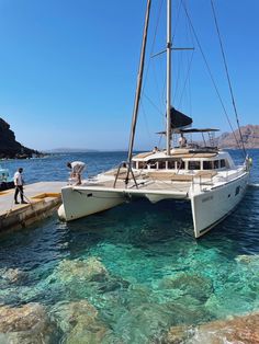 two sailboats docked at the dock in clear blue water with people standing on it