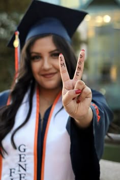 a woman wearing a graduation cap and gown making the v sign with her fingers in front of her