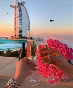 two people toasting with wine glasses in front of the burj hotel and pink roses