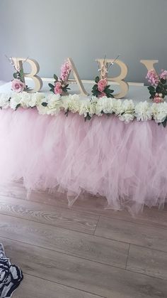 a pink tulle skirted table with flowers and letters on the top that spell out baby