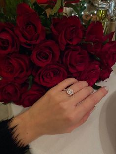 a woman's hand with a diamond ring on her finger next to a bouquet of red roses