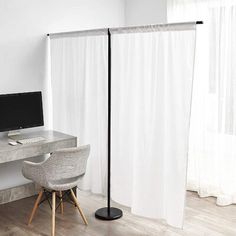 a desk with a laptop on it next to a white curtained wall and chair