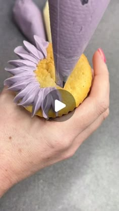 a woman's hand holding a purple cone with yellow and white decorations on it