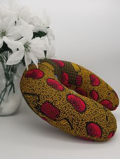 a vase filled with white flowers next to a yellow and red patterned pillow on top of a table