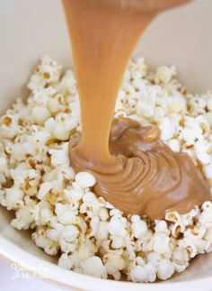 a bowl filled with popcorn and caramel being drizzled on top of it