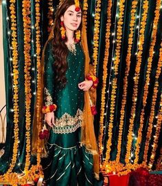 a woman dressed in green and gold standing next to a curtain with flowers on it