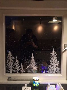 a man is looking out the window at christmas trees and snow falling on the windowsill