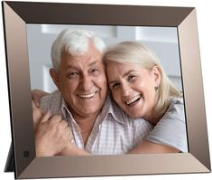 an older man and woman are smiling in front of a silver frame with the image of them