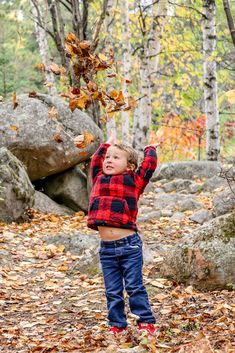 a young boy throws leaves in the air while standing on some rocks and fallen leaves