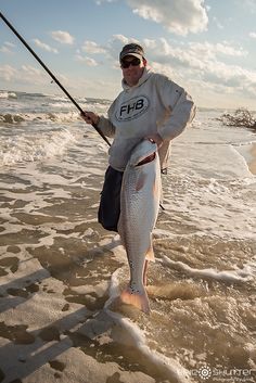 a man holding a fish while standing in the water with a fishing pole and rod