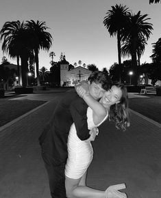 a man and woman are hugging on the sidewalk with palm trees in the back ground