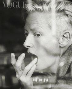 a black and white photo of a woman eating something with her hand in her mouth